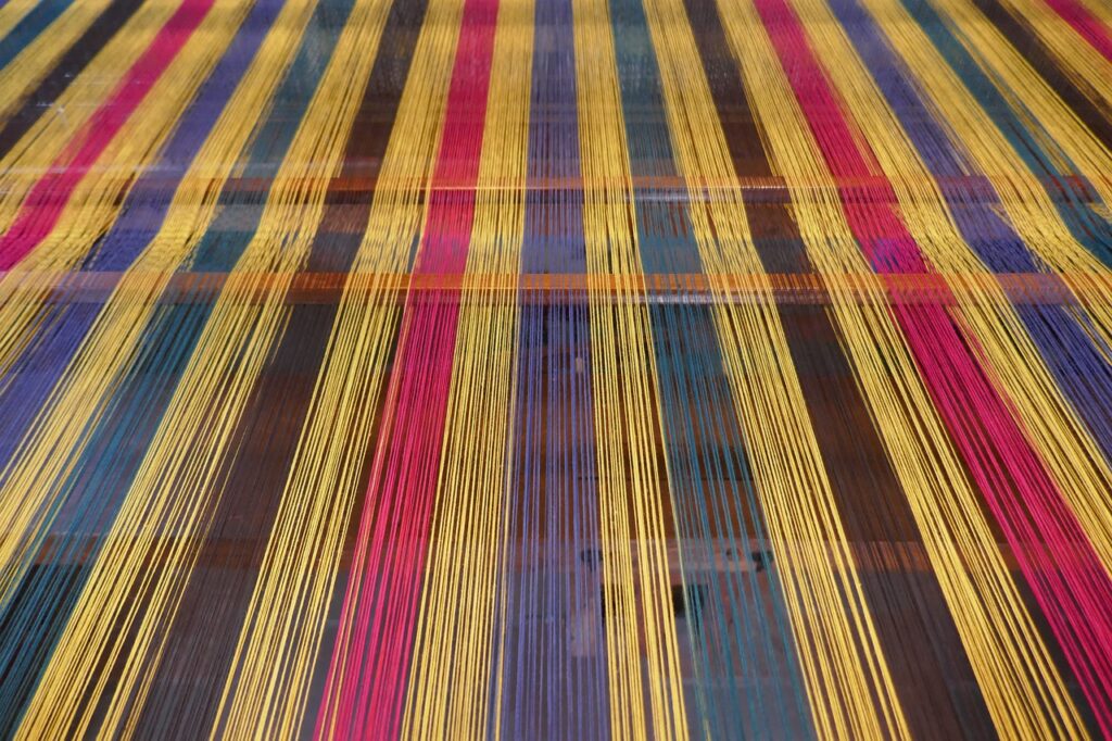 A detailed view of the weaving process of muslin fabric, showing the interlacing of warp and weft threads on a loom, highlighting the craftsmanship involved in creating this lightweight textile.